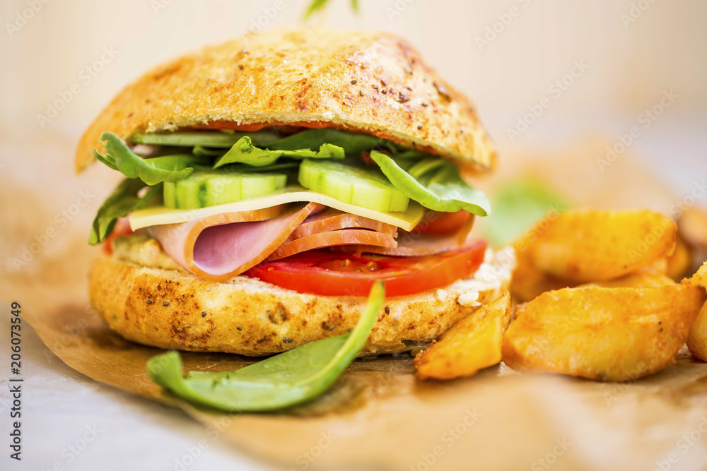 Ham burger or sandwich with ham slices,cheese, cucumbers, tomatoes and lettuce with wedges potatoes, rustic homemade sandwich Ham burger or sandwich with ham slices,cheese, cucumbers, tomatoes and lettuce with wedges potatoes, rustic homemade sandwich