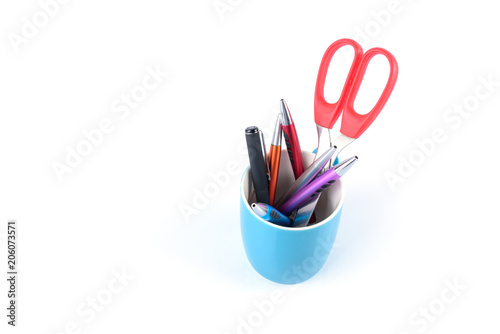 Colorful pens and orange scissors are in blue mug isolated on white background.