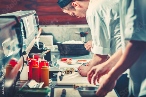 Two young chefs in white uniform preparing sushi set, only hands close up. Interior of modern restaurant kitchen. Food concept. Vintage instagram Color filter toning