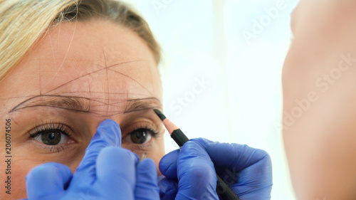 Cosmetologist preparing woman for eyebrow permanent makeup procedure, closeup