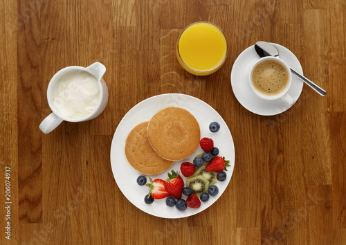 Continental breakfast of a Pancakes, fruit, orange juice, and coffee, shot on a wooden table top, from above.