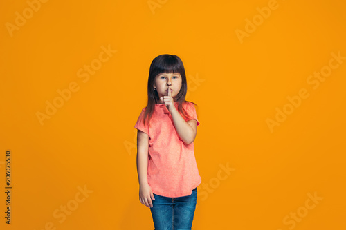 The young teen girl whispering a secret behind her hand over orange background