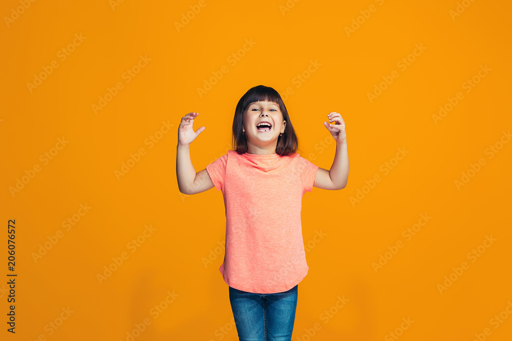 The happy teen girl standing and smiling against orange background. The happy teen girl standing and smiling against orange background.