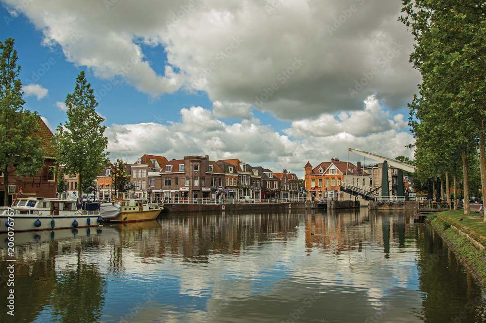 Brick houses, moored boats and bascule bridge reflected in wide canal water surface on sunset in Weesp. Quiet and pleasant village full of canals and green near Amsterdam. Northern Netherlands. 