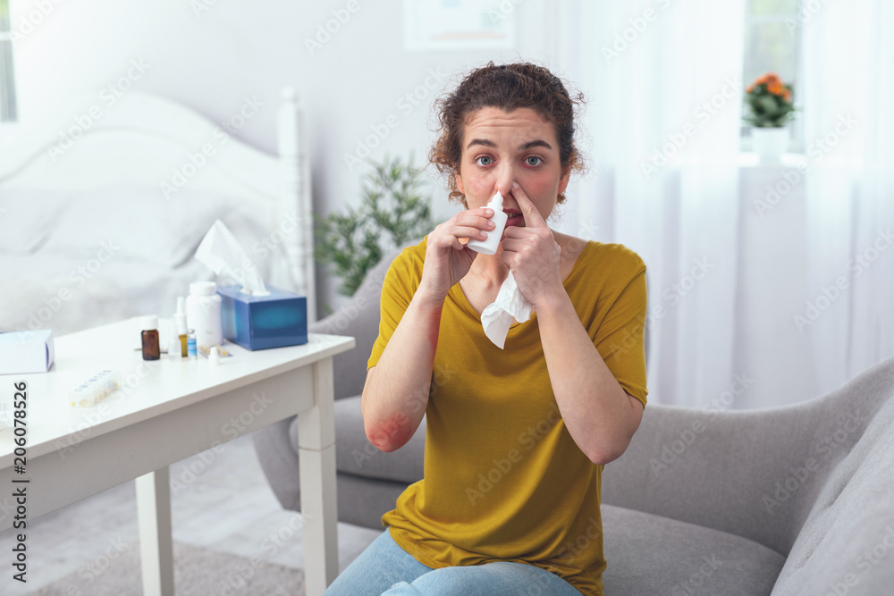 Get well soon. Young sick looking lady feeling unhappy hoping to recover soon while trying to decongest her nose Get well soon. Young sick looking lady feeling unhappy hoping to recover soon while trying to decongest her nose