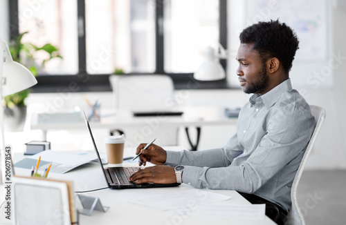 business, people and technology concept - african american businessman with laptop computer working at office