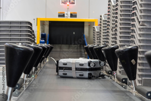 Suitcase on luggage conveyor belt at baggage  handling belt conveyor system at check in desk in airport. Baggage is running on the conveyor belt through an airport safety system.