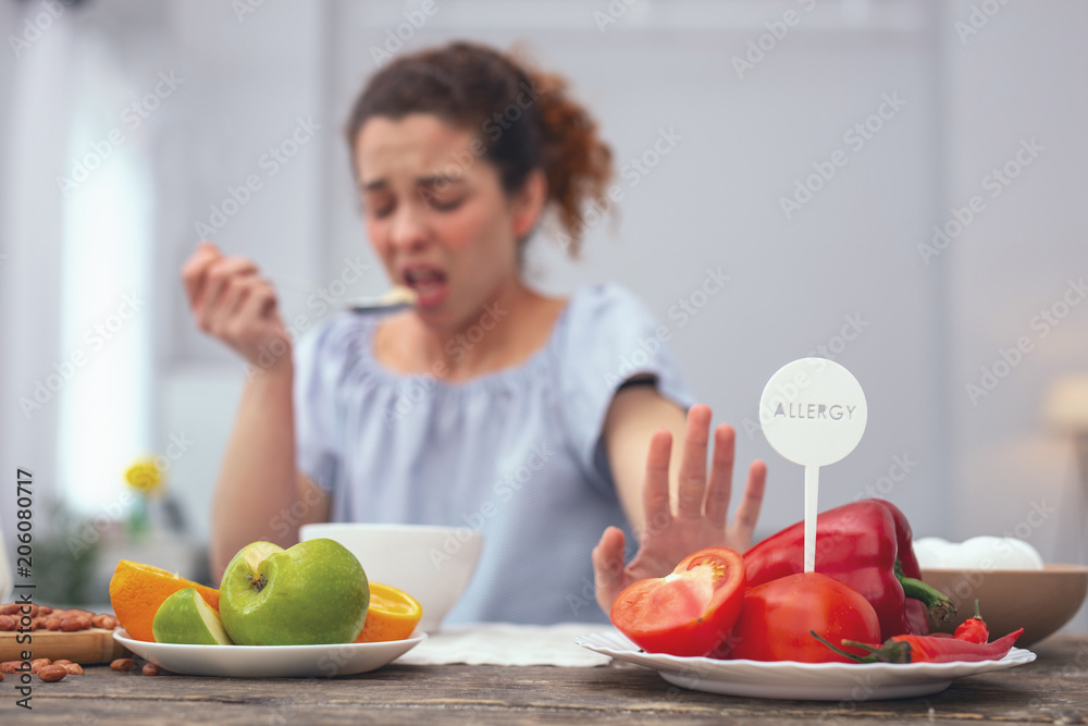 No vegetables. Young woman looking unhappy acting conscious while refusing to consume vegetables which provoke her allergic response No vegetables. Young woman looking unhappy acting conscious while refusing to consume vegetables which provoke her allergic response