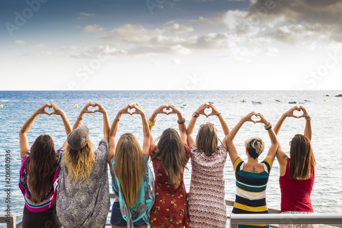 seven girls from the backside doing a heart with the hands looking at the ocean waiting the sunset in vacation leisure activity. friendshipt all together forever concept, travel to sea places