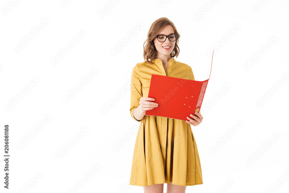 Portrait of pretty smiling lady in eyeglasses and yellow dress standing with red open folder in hand on white background isolated Portrait of pretty smiling lady in eyeglasses and yellow dress standing with red open folder in hand on white background isolated