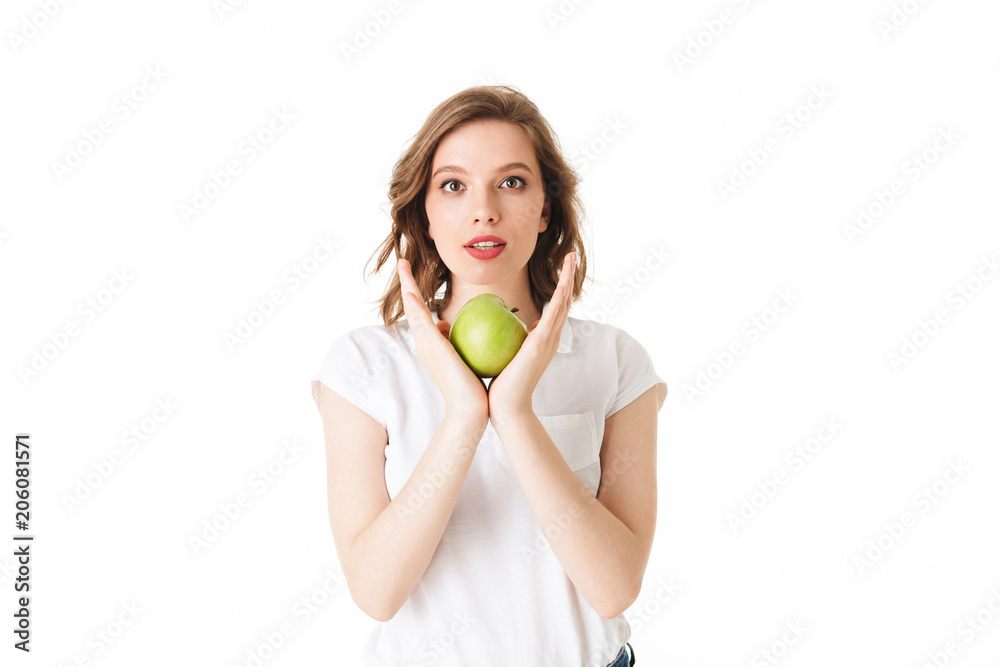 Portrait of young pensive lady standing with green apple in hand and dreamily looking in camera on white background isolated Portrait of young pensive lady standing with green apple in hand and dreamily looking in camera on white background isolated