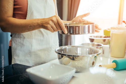 A woman sifting flour into a stainless bowl. Girl is sifting flour to making the bakery in her kitchen on weekend.