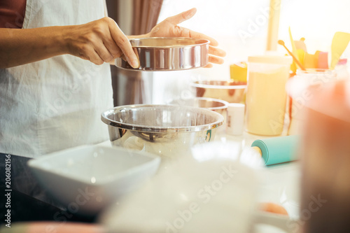 A woman sifting flour into a bowl. Girl is sifting flour to making the bakery in her kitchen on weekend.