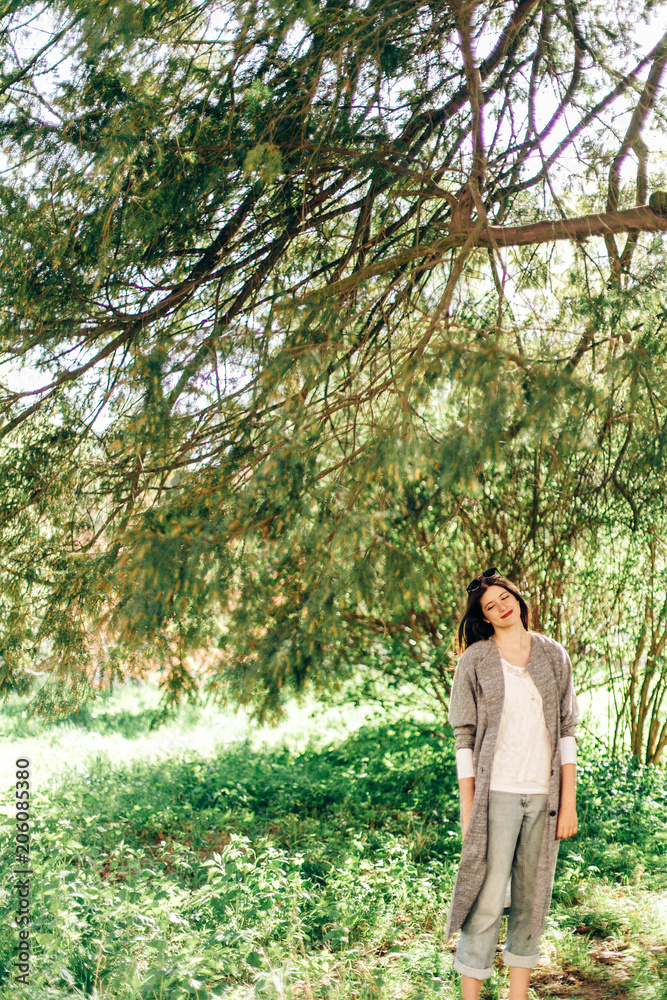 stylish beautiful hipster woman relaxing under green branches in sunny park. young girl with sunglasses smiling in botanical garden in spring. space for text. joyful moment. stylish beautiful hipster woman relaxing under green branches in sunny park. young girl with sunglasses smiling in botanical garden in spring. space for text. joyful moment.
