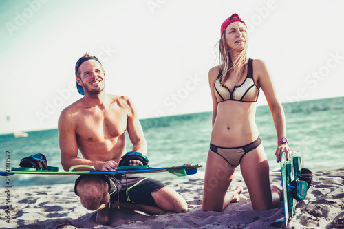 Pretty smiling Caucasian woman kitesurfer enjoying summertime on sandy beach with her boyfriend.
