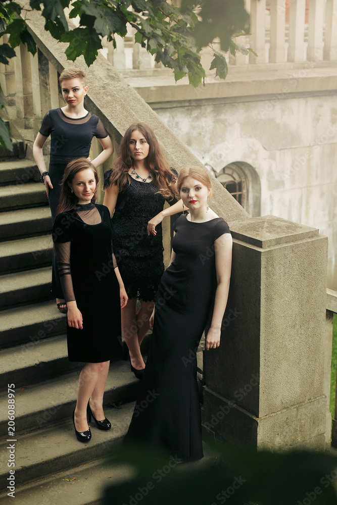 gorgeous luxury  women in black dresses posing smiling on stairs under tree in the city. stylish lady party with gothic theme. elegant girls, view from top