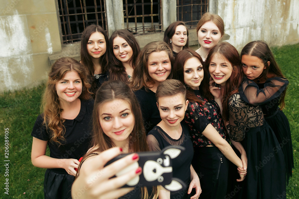 Obraz premium gorgeous women group in black dresses taking selfie having fun and laughing in the city. stylish lady party with gothic theme. elegant girls
