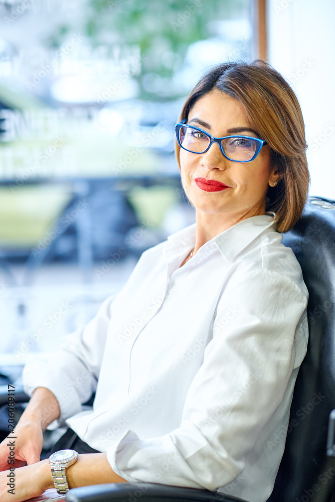 Portrait of a young businesswoman with fair hair smiling and sitting in a leather armchair and with a book in her hands. Concept of business communication. Portrait of a young businesswoman with fair hair smiling and sitting in a leather armchair and with a book in her hands. Concept of business communication.