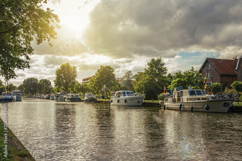 Wide tree-lined canal with houses and boat moored on its bank on sunset at Weesp. Quiet and pleasant village full of canals and green near Amsterdam. Northern Netherlands. Retouched photo.