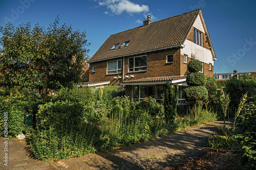 Orange brick house with beautiful and verdant garden in front of alley under blue sky at Weesp. Quiet and pleasant village full of canals and green near Amsterdam. Northern Netherlands.