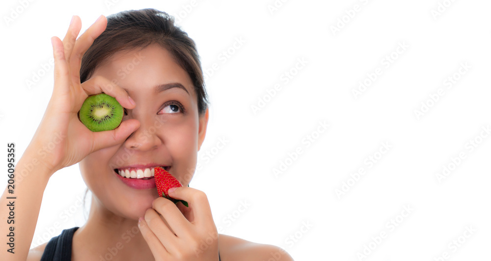 Beautiful woman holding kiwi slice hiding eye. And hold the strawberry at the mouth. Bright red eatable. She looks healthy. She has tan skin. behind isolated on white background. Copy space. Beautiful woman holding kiwi slice hiding eye. And hold the strawberry at the mouth. Bright red eatable. She looks healthy. She has tan skin. behind isolated on white background. Copy space.