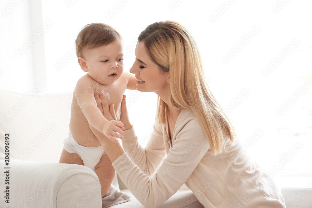 Woman applying body cream on her baby indoors Woman applying body cream on her baby indoors