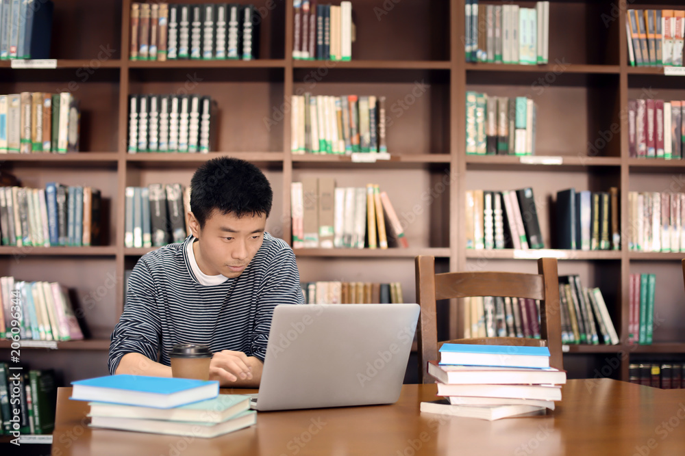Asian student with laptop studying in library Asian student with laptop studying in library