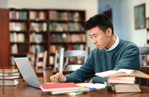 Asian student with laptop studying in library