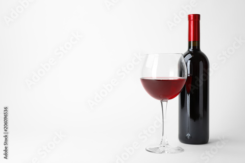 Bottle and glass of expensive red wine on light background
