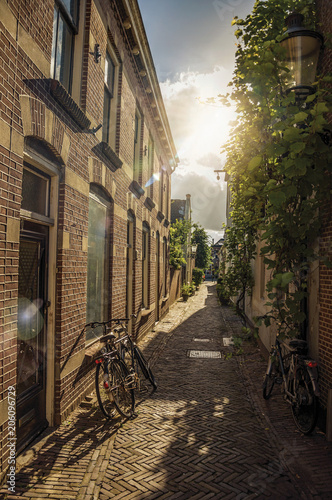 Alleyway with brick houses, bikes and bright sunset light in Weesp. Quiet and pleasant village full of canals and green near Amsterdam. Northern Netherlands. Retouched photo. © Celli07
