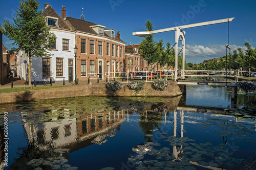 Tree-lined canal with aquatic plants, bascule bridge and brick houses at the bank on sunset in Weesp. Quiet and pleasant village full of canals and green near Amsterdam. Northern Netherlands.