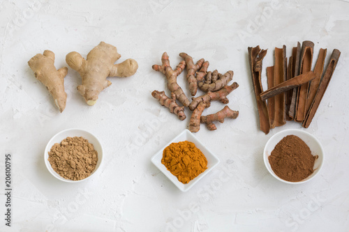 Fototapeta Naklejka Na Ścianę i Meble -  Three healthy spices (turmeric, ginger and cinnamon) in white bowls on white concrete background