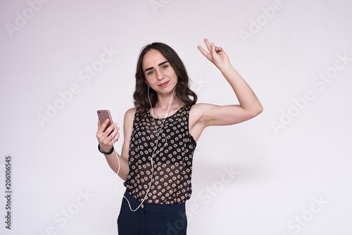 Portrait of a beautiful young brunette girl over a white background listening to music in headphones with a smartphone. © Вячеслав Чичаев