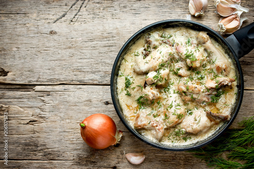 Gedlibzhe — kabardian chicken in sour cream sauce with onion in a frying pan on a wooden background