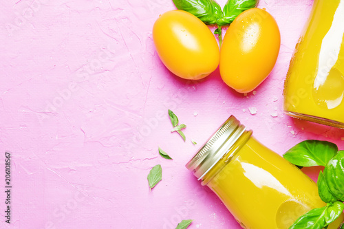 Useful and healthy smoothie or juice from yellow tomatoes and bell peppers with green basil and oregano in glass bottles, pink background, top view photo