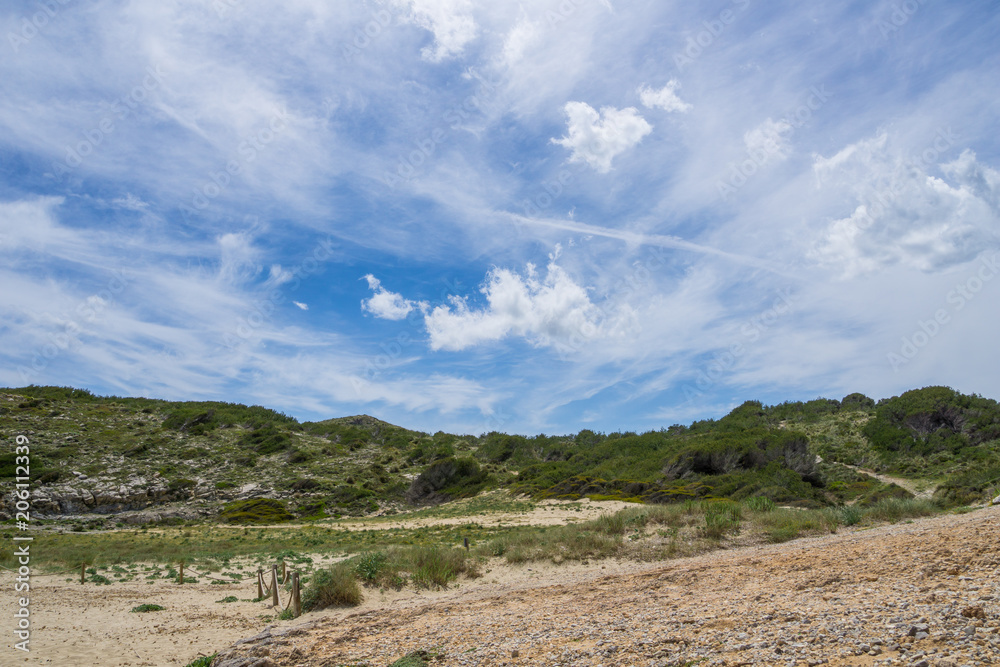 Mallorca, Hike trails through green ground vegetation near Cala Mitjana bay with blue sky