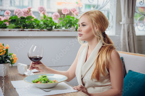 Young blonde woman drinking red wine in an outdoor restaurant