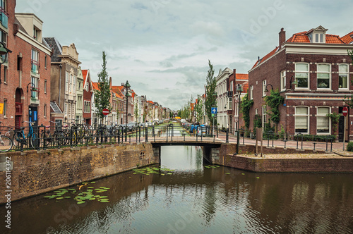 Tree-lined long canal with small bridge, brick houses on its bank and cloudy day at Gouda. Very popular day trip destination, is famous for its tasty Gouda cheese. Southern Netherlands.