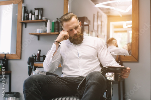 Portrait of handsome bearded man with fashionable hairstyle and beard at barber shop. He chooses a haircut in the journal. © anatoliycherkas