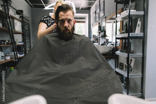 Stylish hairdresser cutting hair of client at barber shop. Beard man getting haircut at salon.