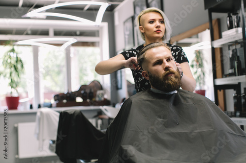 Stylish hairdresser cutting hair of client at barber shop. Beard man getting haircut at salon.