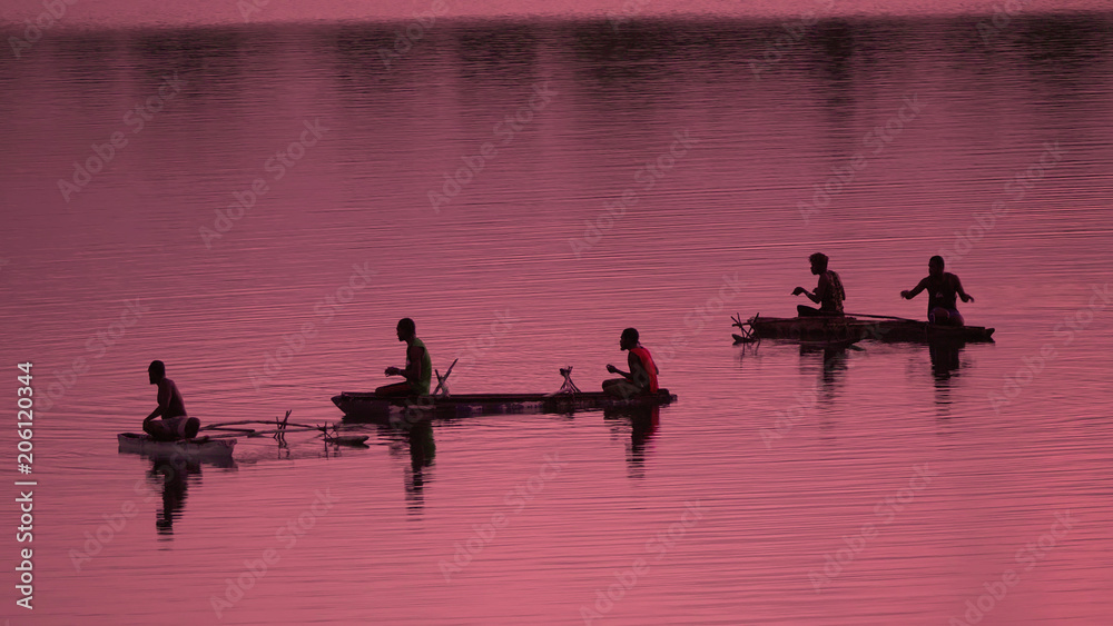 Naklejka premium SILHOUETTE Unrecognizable local fishermen fishing in small boats at pink sunrise