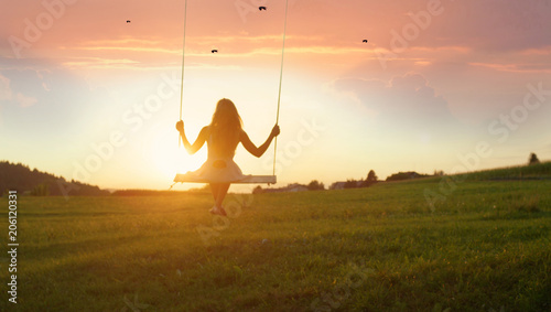 SILHOUETTE: Unrecognizable young woman swaying on swing at golden summer sunset