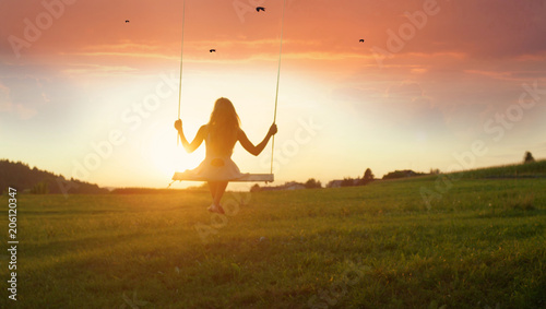 SILHOUETTE: Unknown girl swaying on wooden swing at golden sunset in spring