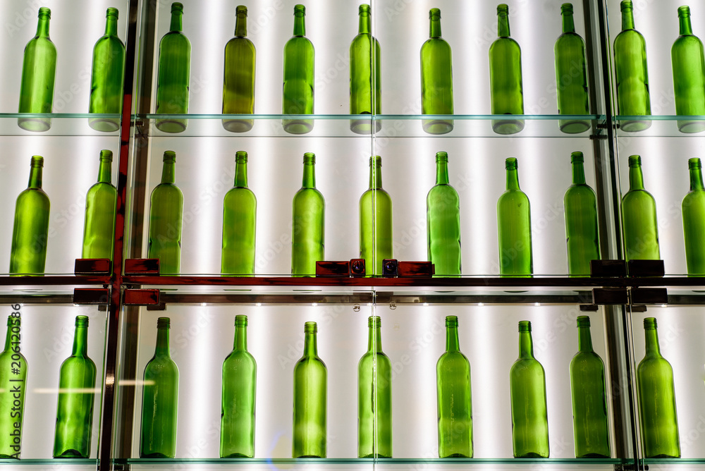 rows of empty green wine bottles line glass shelves set against a wall