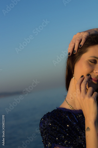beautiful brazilian woman with brown hair and wearing bright blue fashion blouse and touching her face while enjoying sunshine