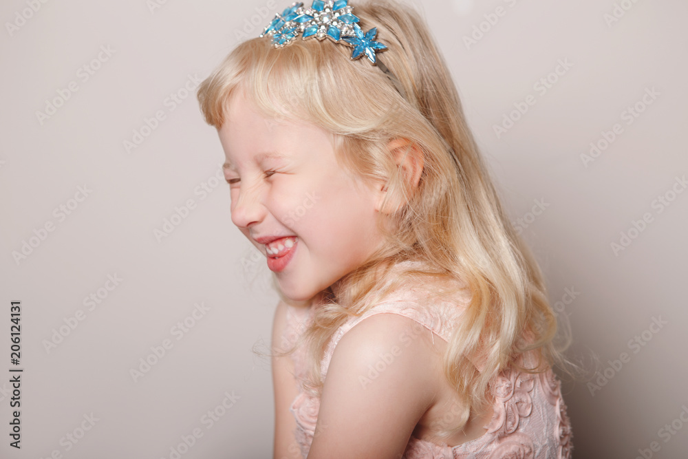 Closeup portrait of cute adorable white blonde fair Caucasian preschool girl in pink dress and princess crown. Child smiling laughing posing in studio on plain light background. Closeup portrait of cute adorable white blonde fair Caucasian preschool girl in pink dress and princess crown. Child smiling laughing posing in studio on plain light background.