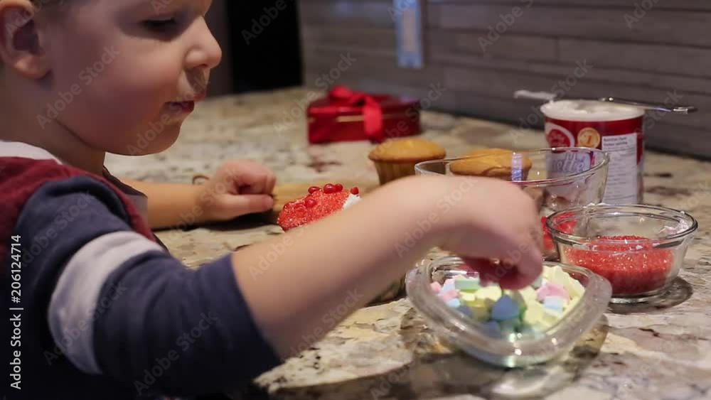 little boy puts candy heart on valentines cupcake little boy puts candy heart on valentines cupcake