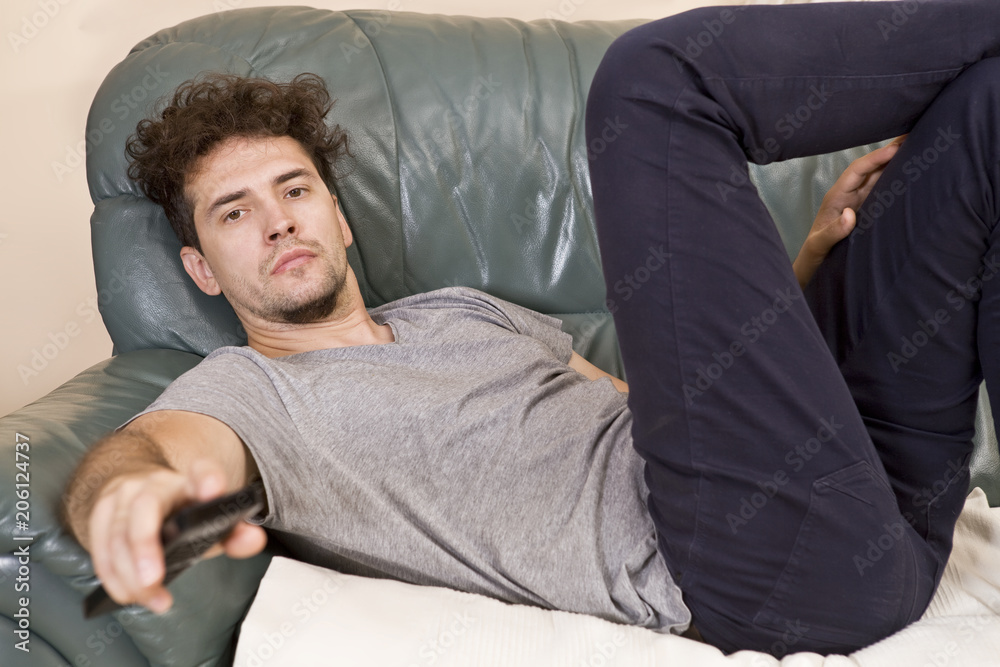 Fototapeta premium A young man watches television and changes channels while relaxing
