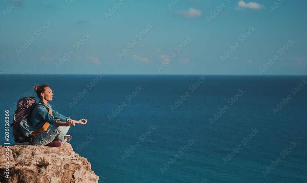 Profile of enjoyed camper relaxing on stony mountain in yoga pose. Blue ocean on background